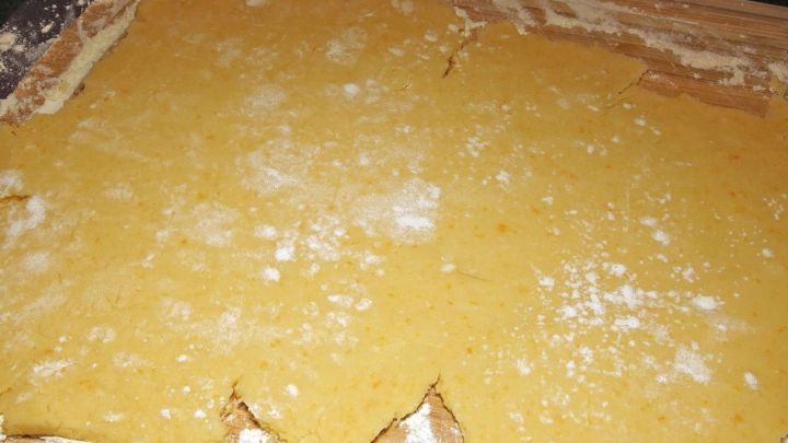 M&uuml;rbeteig ist ausgerollt auf einem Holzbrett, umgeben von etwas Mehl, bereit zum Backen oder Weiterverarbeiten.