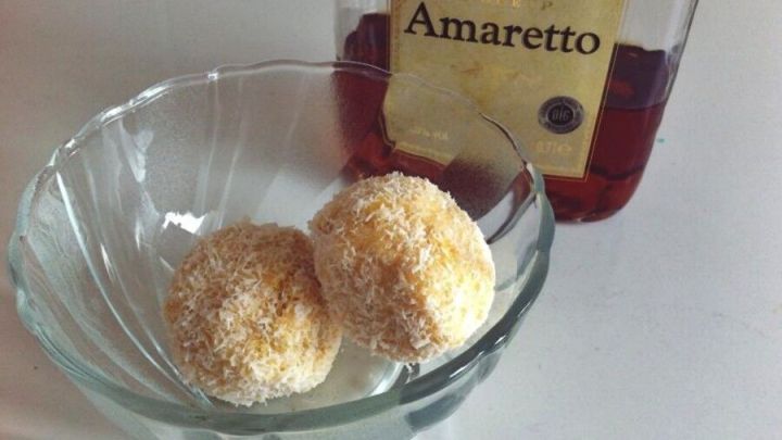 Zwei runde Schneeb&auml;lle mit Amaretto liegen in einer Glas-Sch&uuml;ssel, umgeben von einer Flasche Amaretto in einem hellen Raum.