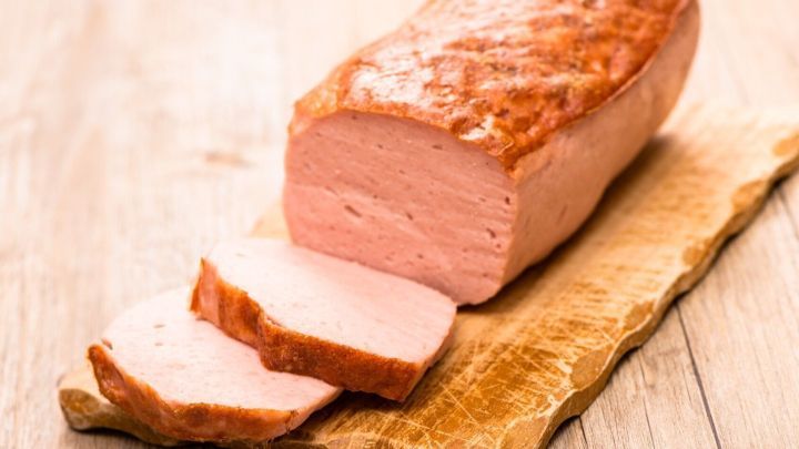 Eine Leberk&auml;s-Salzst&uuml;ck liegt auf einem Holzbrett, w&auml;hrend einige Scheiben appetitlich geschnitten daneben liegen.