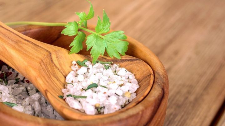 Feines Liebst&ouml;ckel-Salz in einer Holzschale wird mit einem L&ouml;ffel serviert, umgeben von einer sch&ouml;nen Holzoberfl&auml;che.