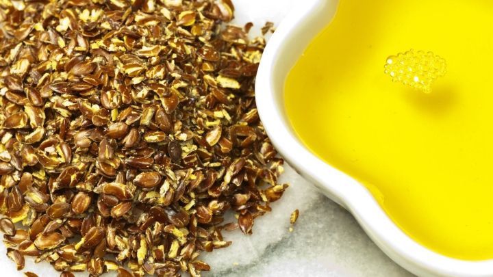 Lein&ouml;l steht in einer Schale neben gemahlenen Leinsamen, die auf einem wei&szlig;en Untergrund liegen, und betont die Verwendung von &Ouml;l.