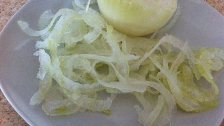 Hauchd&uuml;nne Zwiebelscheiben liegen auf einem Teller, w&auml;hrend eine unzerkleinerte Zwiebel daneben steht.