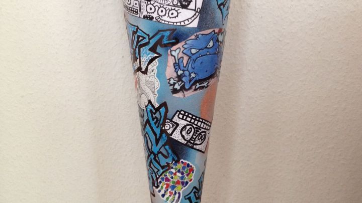Eine bunte Schult&uuml;te im Graffiti-Look steht auf einem Holzfu&szlig;boden, dekoriert mit stilisierten Zeichnungen und Farben.