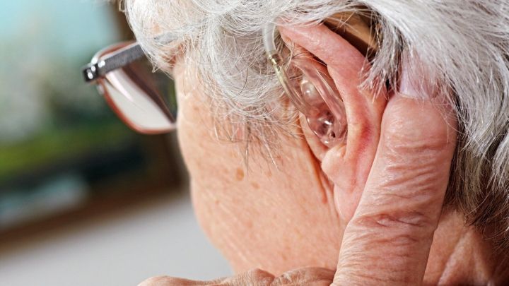 Eine &auml;ltere Person mit einer Brille hat ein H&ouml;rger&auml;t im Ohr und zieht vorsichtig an ihrem Ohr.