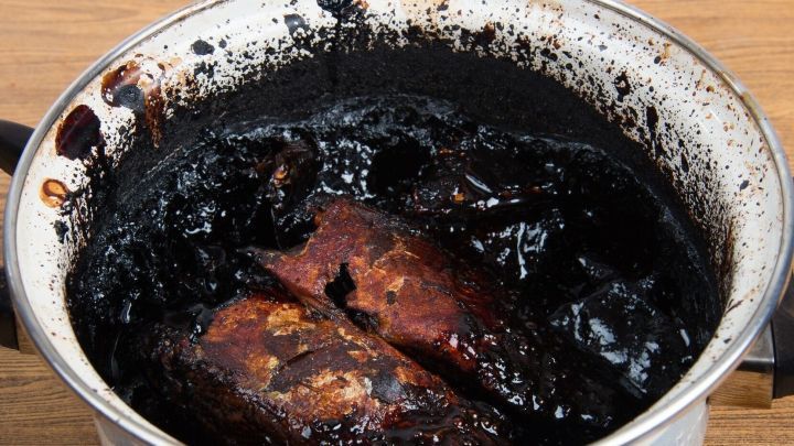 Ein stark angebrannter Topf liegt auf einem Tisch, der schwarze Belag zeigt die Herausforderung beim Reinigen mit Backpulver.