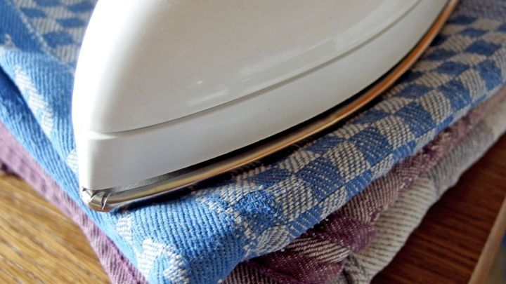 Ein wei&szlig;es B&uuml;geleisen ruht auf einem Stapel von bunten Geschirrt&uuml;chern, in einer gem&uuml;tlichen K&uuml;chenecke.