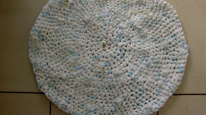 Ein runder Badteppich aus upgecycelten Materialien liegt auf einem hellen Fliesenboden und zeigt eine feine, geh&auml;kelte Struktur.