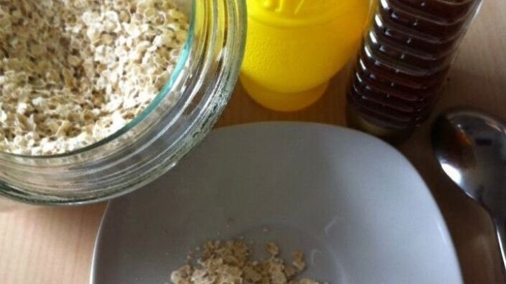 Haferflocken liegen auf einem Teller, w&auml;hrend ein Glas Haferflocken, eine gelbe Flasche und ein &Ouml;ldosierer im Hintergrund stehen.