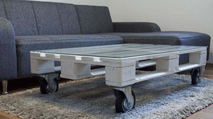 Ein stylischer Couchtisch aus Europaletten mit Rollen steht auf einem Teppich, neben einem modernen grauen Sofa in einem Wohnraum.