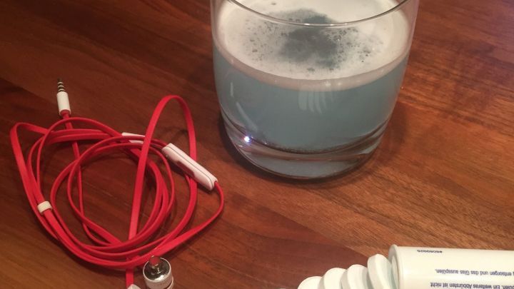 Zwei Ohrst&ouml;psel liegen neben einer Tube und einem Glas blauer Fl&uuml;ssigkeit auf einem Tisch, bereit zur Reinigung.