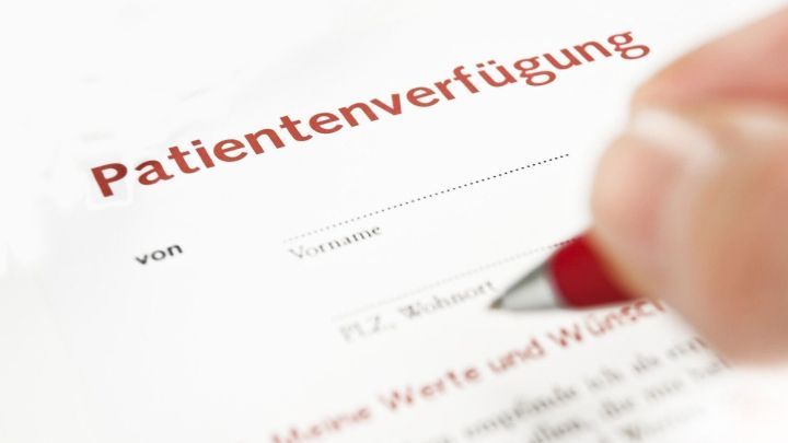 Ein Dokument mit dem Titel "Patientenverf&uuml;gung" wird von einer Hand mit einem roten Stift unterschrieben, um wichtige W&uuml;nsche festzuhalten.