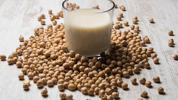 Ein Glas Soja-Drink steht auf einem Haufen von Sojabohnen und zeigt pflanzliche Alternativen zur Milch in einer hellen Umgebung.