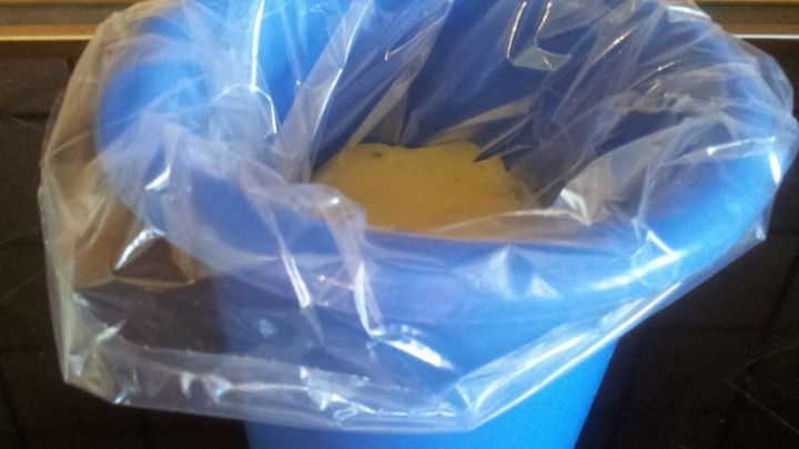 Ein blauer Eimer mit einer durchsichtigen Plastikfolie oben drauf steht auf einer Kochplatte, bereit zum Suppe einfrieren ohne Kleckern.