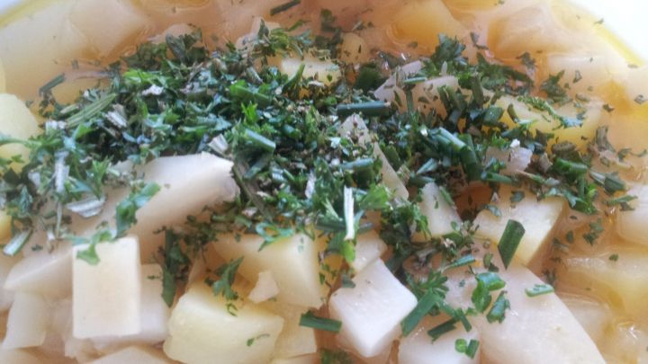 Ein Eintopf mit st&uuml;ckigen Gem&uuml;se und frischen Kr&auml;utern wird in einer wei&szlig;en Sch&uuml;ssel serviert.