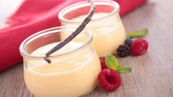 Zwei Gl&auml;ser mit fruchtiger Erfrischungscreme stehen auf einem Holztisch, umgeben von frischen Beeren und einem roten Tuch.