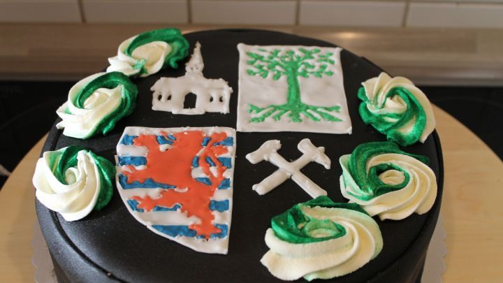 Eine schwarze Torte dekoriert mit Royal Icing, kunstvollen Rohlingen und Wappenmuster, steht auf einem Tisch.