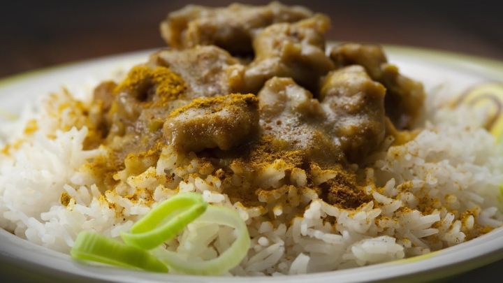 Ein Teller mit libanesischem Reis, bedeckt mit w&uuml;rzigem Fleischragout und dekoriert mit Lauchringen, steht auf einem Tisch.