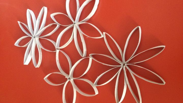 Blumen aus leeren Klopapierrollen sind kreativ angeordnet und heben sich vor einem roten Hintergrund ab.