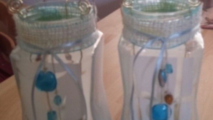 Zwei dekorative Windlichter aus NC-Gl&auml;sern stehen auf einem Holzstamm und zeigen bunte Anh&auml;nger im Raum.