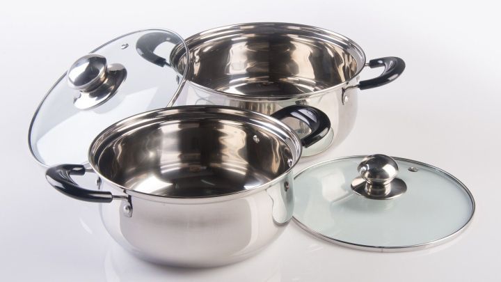 Zwei gl&auml;nzende T&ouml;pfe aus Edelstahl liegen &uuml;bereinander, w&auml;hrend der Deckel teilweise abgenommen ist, auf einem wei&szlig;en Untergrund.