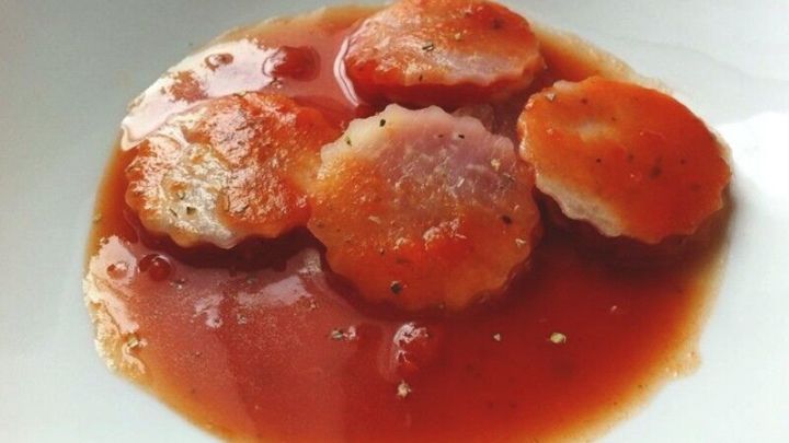 Kohlrabi-Ravioli liegen in einer Tomaten-Basilikum-So&szlig;e auf einem wei&szlig;en Teller und sind appetitlich angerichtet.