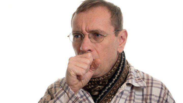 Ein Mann hustet, w&auml;hrend er einen Schal tr&auml;gt. Er hat eine bem&uuml;hte Miene und schaut nachdenklich, was auf Unwohlsein hinweist.