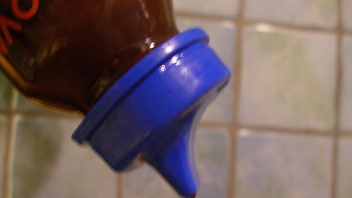 Ein Babyfl&auml;schchen wird &uuml;ber einer Fliese gehalten, w&auml;hrend es Salatdressing auf einen Teller verteilt.