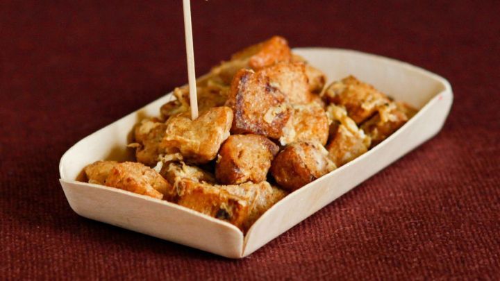 Kleine, knusprige Brotw&uuml;rfel liegen auf einem wei&szlig;en Teller mit einem Holzspie&szlig;, serviert auf einem rotbraunen Tisch.