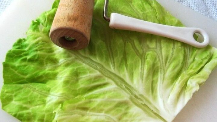 Ein frisches Kohlblatt liegt auf einem Schneidebrett, w&auml;hrend ein Rollger&auml;t es sanft plattiert, um bei Gelenkschmerzen zu helfen.