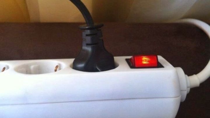 Eine Steckdosenleiste mit einem schwarz angeschlossenen Kabel und einem roten Schalter, liegt auf einem braunen Stoff.