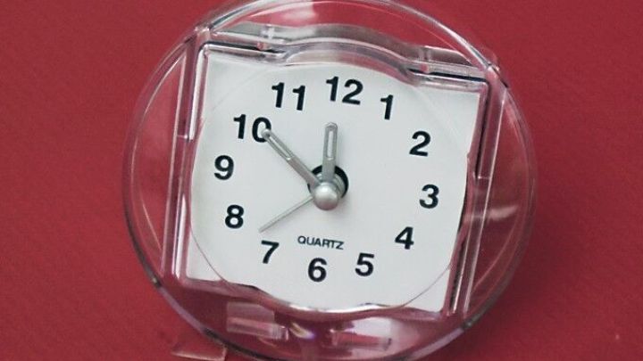 Eine klare Tischuhr zeigt die Zeit an und steht auf einem roten Untergrund, was den Fokus auf die Zeitmessung betont.