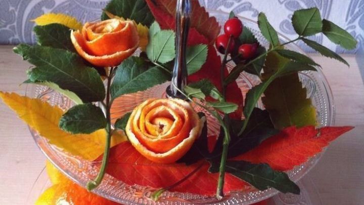 Mit Rosen aus Mandarinenschalen geschm&uuml;ckter Obstst&auml;nder zeigt eine herbstliche Dekoration mit Mandarinen und buntem Laub.