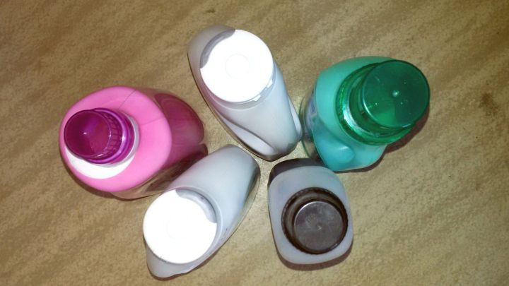 F&uuml;nf Flaschen Waschmittel in verschiedenen Farben stehen auf einem Holzuntergrund, bereit zur Verwendung f&uuml;r moderne Waschmittel.