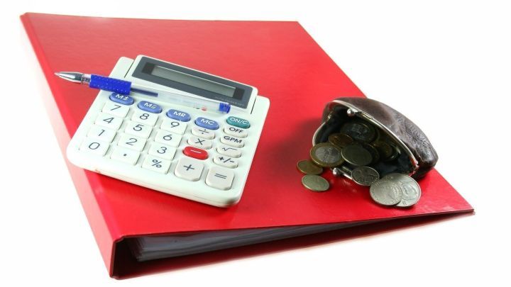 Ein roter Haushaltsordner liegt auf einem Tisch, daneben ein Taschenrechner und ein offenes Geldb&ouml;rsen mit M&uuml;nzen.