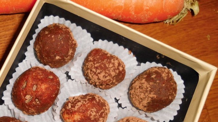 In einer Schachtel liegen Marzipankartoffeln, w&auml;hrend daneben frische Karotten auf einem Holzuntergrund liegen.