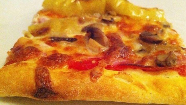 Ein knuspriger Pizzaboden mit geschmolzenem K&auml;se und Gem&uuml;se liegt auf einem wei&szlig;en Teller und verf&uuml;hrt mit seinem Aroma.
