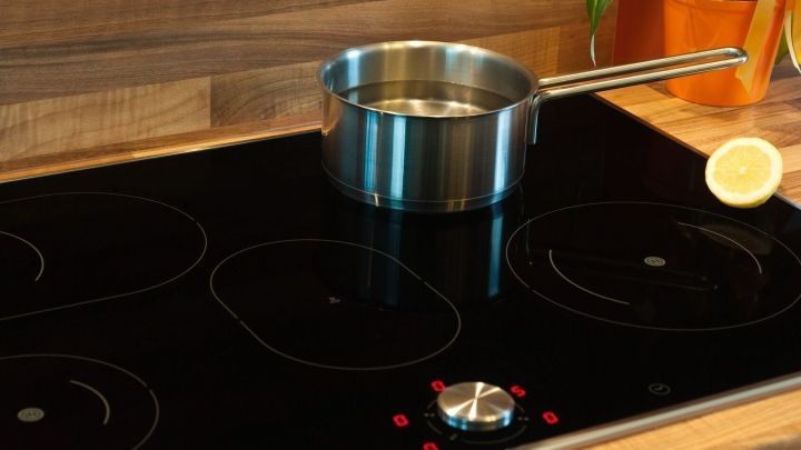 Ein Topf mit Wasser erhitzt sich auf einem modernen Induktionsherd in einer gem&uuml;tlichen K&uuml;chenumgebung mit Holzregal.