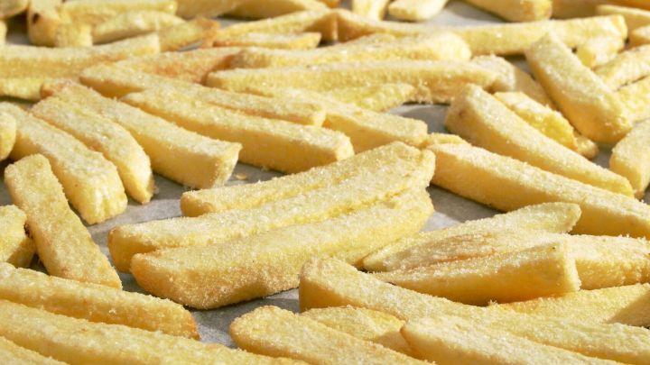 Knusprige backofenfrische Pommes liegen gleichm&auml;&szlig;ig auf einem Blech, bereit zum Backen in einer heimischen K&uuml;che.