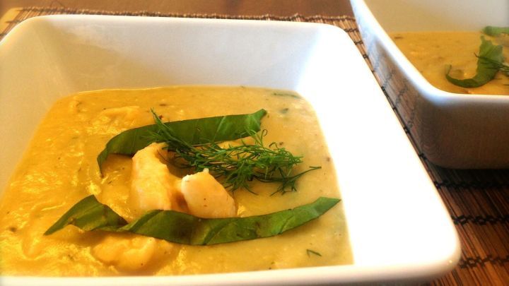 Eine cremige Kartoffelsuppe mit Lachs, Basilikum und Dill, serviert in einer wei&szlig;en Sch&uuml;ssel auf einem Holzuntergrund.