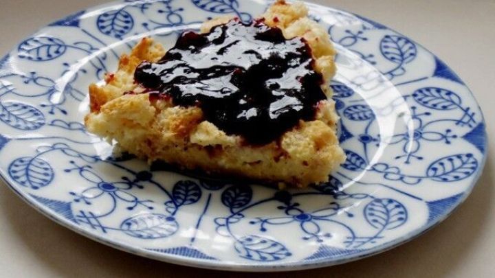 Ein St&uuml;ck Zwieback Auflauf mit dunkler Fruchtso&szlig;e liegt auf einem Teller mit blauem Muster auf wei&szlig;em Hintergrund.