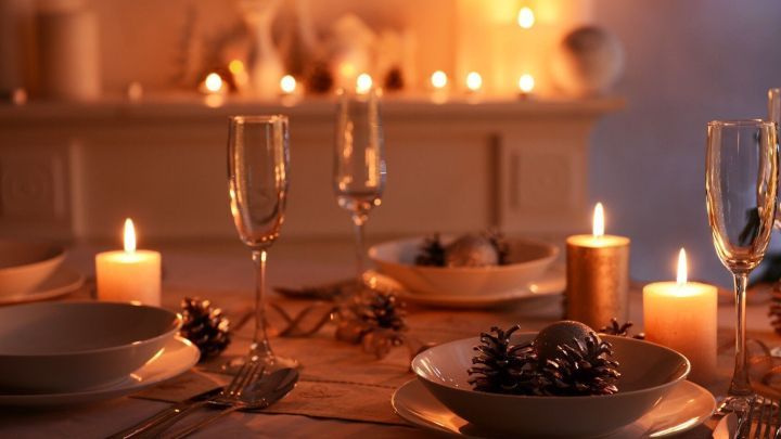 Ein festlich gedeckter Tisch mit Tellern und Gl&auml;sern, umgeben von Kerzenlicht f&uuml;r ein (fast) stressfreies Weihnachten.