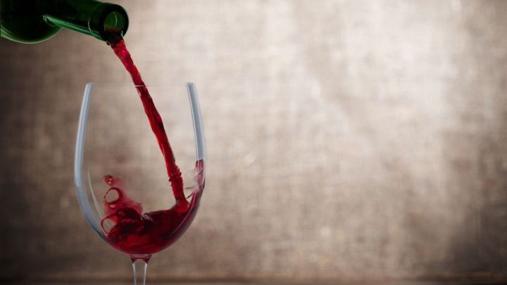 Ein Glas Rotwein wird aus einer Flasche gef&uuml;llt, w&auml;hrend ein unscharfer, heller Hintergrund eine gem&uuml;tliche Atmosph&auml;re schafft.