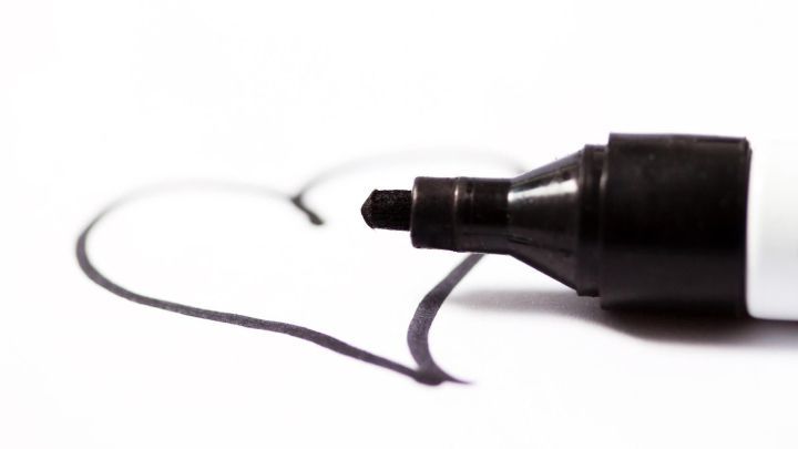 Ein schwarzer Filzschreiber zeichnet ein Herz auf wei&szlig;em Papier.