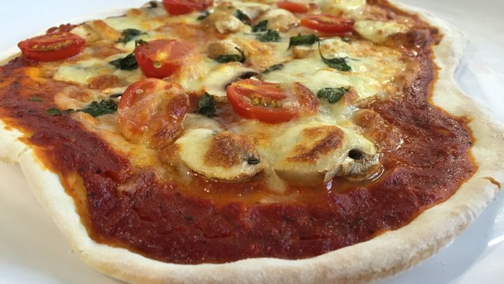 Eine frisch gebackene Pizza liegt auf einem Teller, garniert mit Tomaten und Käse, in einer modernen Küchenumgebung.