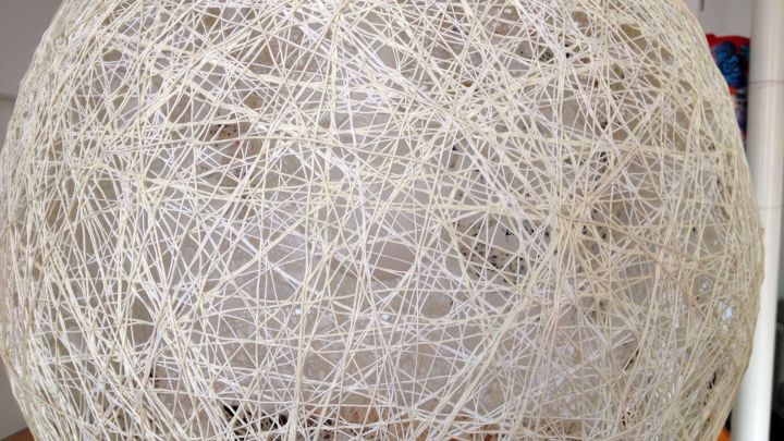 Eine gro&szlig;e H&auml;ngeleuchte aus Wolle h&auml;ngt in einem Raum und zeigt ein kunstvolles Netz aus F&auml;den, das Licht diffundiert.