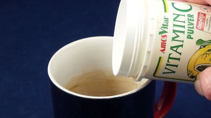 Ein Hand h&auml;lt eine Dose mit Vitamin C Pulver und gie&szlig;t es in eine Tasse, um Teer&auml;nder zu bek&auml;mpfen.