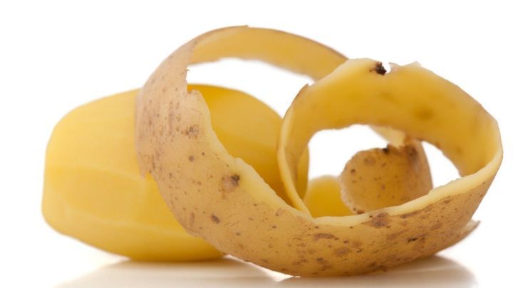Ein Kartoffelschalenst&uuml;ck liegt neben einer gesch&auml;lten Kartoffel und k&ouml;nnte zur Beseitigung von Zwiebelgeruch an den H&auml;nden verwendet werden.