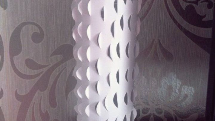 Eine wei&szlig;e Vase mit ausgeschnittenem Muster steht auf einem Regal vor einer kunstvoll gemusterten Tapete.