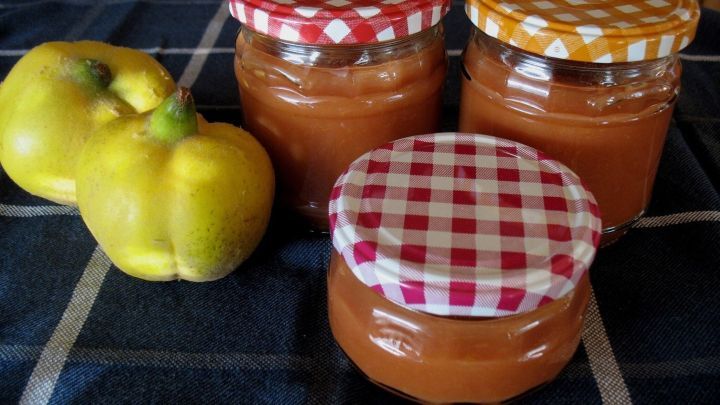 Drei Gl&auml;ser mit Quittenkonfit&uuml;re stehen auf einem blauen Tuch, neben gelben Quitten, die frisch zubereitet wurden.