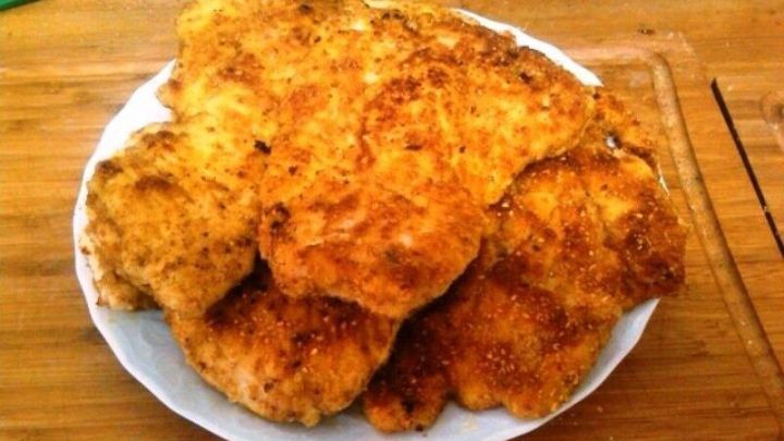 Eine große Portion goldbraun panierter Putenschnitzel liegt appetitlich auf einem weißen Teller in einer Küche.